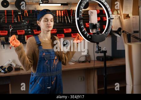 Calmness woman repairman vlogger filming video with ring light in her garage workshop meditating in yoga pose. content for online repairs vlog. Vlogge Stock Photo