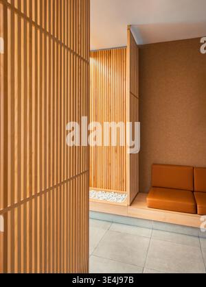 A modern interior space featuring vertical wooden slats and a comfortable brown leather sofa, with a minimalist design and natural elements, creating Stock Photo
