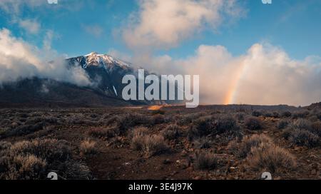 Scenic winter view of Teide National Park in Tenerife, Canary Islands, showcasing a snow-capped volcano under a blue sky with clouds and a rainbow arc Stock Photo
