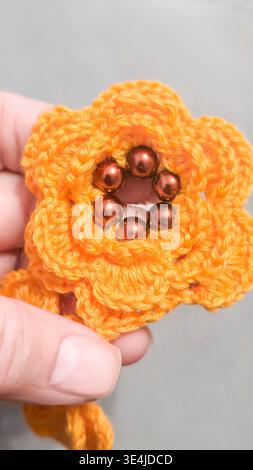 Orange crochet flowers decorated with beads are arranged on a gray background. Handicrafts, textile decor, and handicraft elements in close-up. Clothi Stock Photo