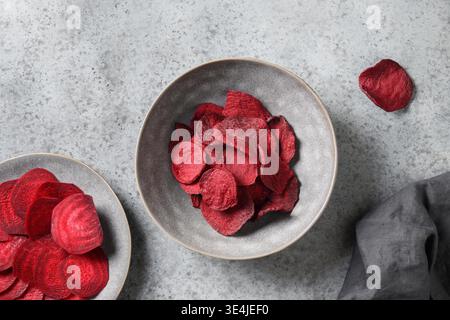 Vegetable beetroot chips in gray bowl on a gray background. Vegan snack. Top view. Home drying, Stock Photo