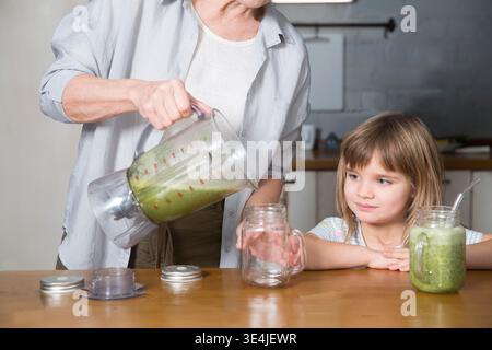 Healthy nutrition in the family, vegetarianism. Senior lifestyle. grandmother and granddaughter drink smoothie from greenery and superfoods in the kitchen at home || Model released Stock Photo
