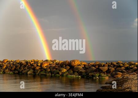Beautiful double rainbow over the sea and stone pier for presentation and background, spectacular nature landscape with stormy sky Stock Photo