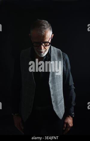 portrait of a mature man looking down on black background Stock Photo