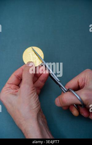Hands cutting a Bitcoin coin with scissors, symbolizing cryptocurrency loss, risk, and financial uncertainty in digital markets Stock Photo