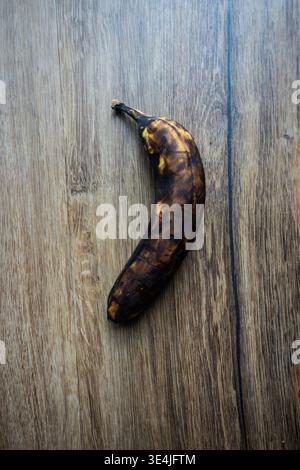 Overripe banana with dark spots on wooden surface, illustrating food waste, spoilage, and natural decay in a minimal still life scene Stock Photo