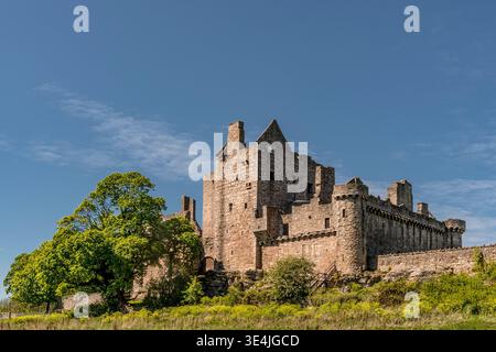 Historic Craigmillar Castle bathed in bright sunlight, showing weathered stone walls, towers and surrounding greenery against a clear blue sky — evoki Stock Photo
