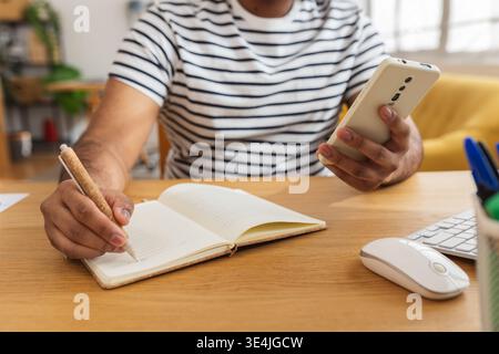 Young Indian man using mobile phone and writing notes Stock Photo