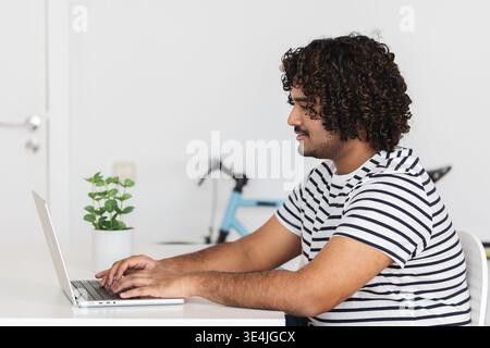 Young Indian man typing on laptop side view Stock Photo