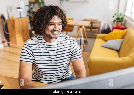 Young Indian man working on desktop PC while studying at desk Stock Photo