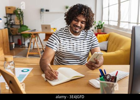 Young Indian man writing notes and checking phone Stock Photo