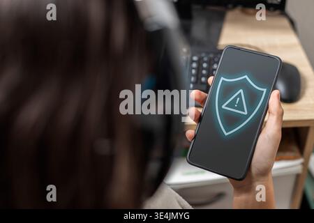 Teenager holding a smartphone displaying a security shield with an exclamation mark Stock Photo