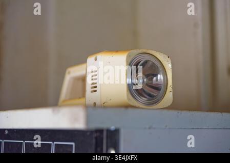 An old white beige flashlight covered in dust and dirt resting on a metal surface indoors with a blurred background, showing signs of wear and age. Stock Photo