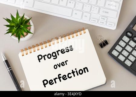 Progress over perfection. Sentence written in a notebook on a desk in an office. Business concept. Close up. Flat lay Stock Photo