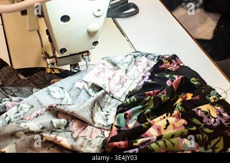 Colorful patchwork fabric being sewn on industrial sewing machine in tailoring workshop, handmade clothing production process close up Stock Photo