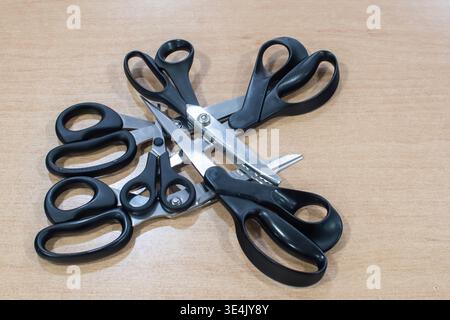 Various sewing scissors arranged on wooden table in tailoring workshop, tools for cutting fabric and handmade clothing production Stock Photo