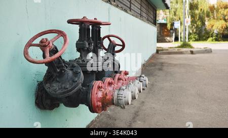 Industrial pipes and valves on building wall for water supply system outdoors Stock Photo