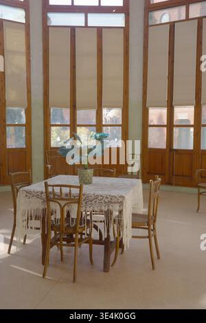 Sunlit period room with Thonet bentwood chairs and lace-covered table beside tall wooden windows at Recinte Modernista de Sant Pau, Barcelona Stock Photo