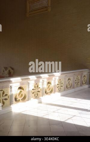Sunlit carved stone balustrade with cross and quatrefoil motifs casting geometric shadows on white marble floor inside Recinte Modernista de Sant Pau Stock Photo