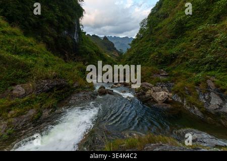 Du Gia, Ha Giang Province, Vietnam – January 18, 2024: A rocky stream flows through a narrow green valley below Du Gia Waterfall. Stock Photo