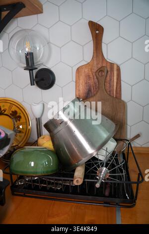 Kitchen dish rack with cookware, cutting board, utensils and wall lamp on hexagon tile background, home kitchen organization scene. Kitchen storage Stock Photo