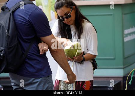 BANGKOK, THAILAND-MAR 15, 2026: Female tourist eating fresh coconut at outdoor market in Bangkok, front view Stock Photo