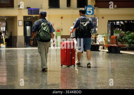 BANGKOK, THAILAND-MAR 15, 2026: Male backpackers walking and dragging luggage at a train station at Hua Lamphong, rear view Stock Photo