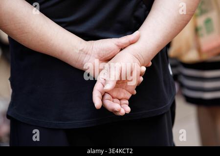 Man standing with hands clasped behind back in relaxed pose, skin texture of hands, unposed movement, natural candid motion, close up Stock Photo