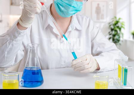 Laboratory technician using pipette to transfer blue liquid into test tube, chemical research and scientific experiment in controlled environment Stock Photo