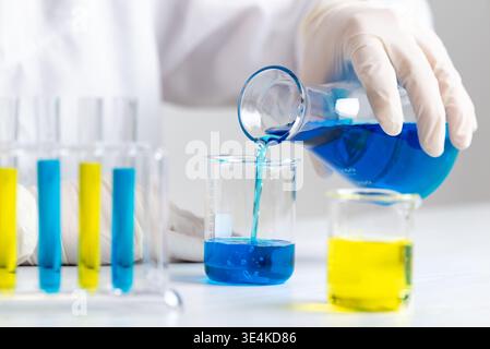 Scientist pouring blue liquid from flask into beaker, laboratory experiment and chemical mixing process in controlled environment Stock Photo