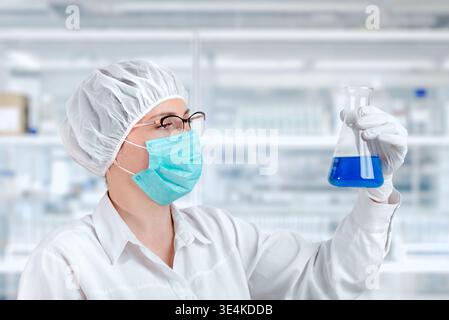 Laboratory technician analyzing blue liquid in flask, scientific research and chemical testing in controlled lab environment Stock Photo
