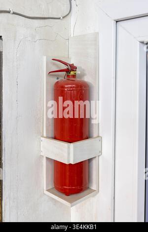 A red fire extinguisher cylinder for fire safety on the wall of the room near the exit door Stock Photo