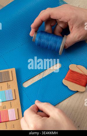 A master tanner works with leather, creating a blue leather bag. The hands of a master leatherworker. Stock Photo