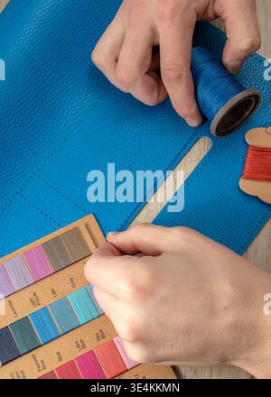 A master tanner works with leather, creating a blue leather bag. The hands of a master leatherworker. Stock Photo