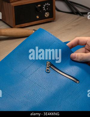 A master tanner works with leather, creating a blue leather bag. The hands of a master leatherworker. Stock Photo