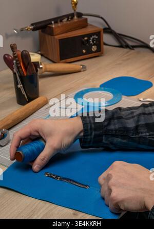 A master tanner works with leather, creating a blue leather bag. The hands of a master leatherworker. Stock Photo