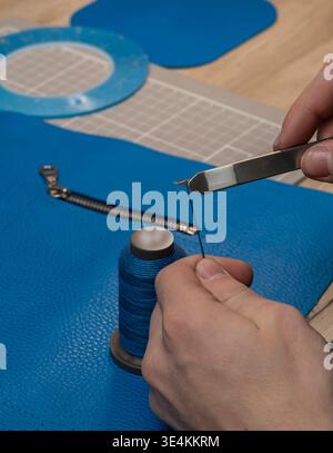 A master tanner works with leather, creating a blue leather bag. The hands of a master leatherworker. Stock Photo