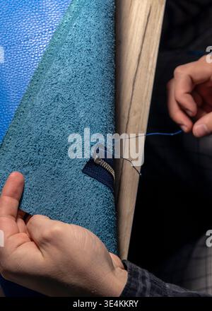 A master tanner works with leather, creating a blue leather bag. The hands of a master leatherworker. Stock Photo