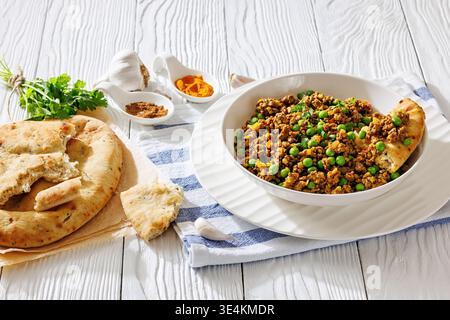 Keema Matar, hearty curry with minced lamb meat and peas in a bowl served with naan bread and spices on white wooden table, Indian cuisine, horizontal Stock Photo