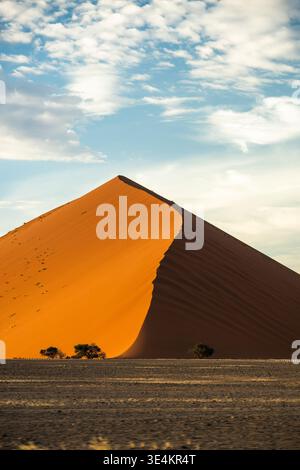 Steep Sand Dune With Footprints Climbing Ridge, Dramatic Golden Slope Under Textured Sky, Sense Of Journey Stock Photo