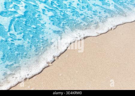 Close-up of a foamy sea wave meeting soft sand on a tropical beach. Clean and versatile background for summer, travel, resort and wellness themes. Stock Photo