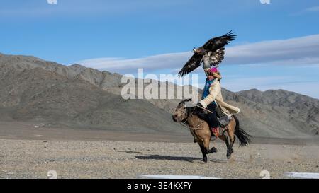 Side view of a Mongolian eagle hunter (berkutchi) riding a horse with a blindfolded golden eagle, Altai Mountains, Bayan-Olgii, Western Mongolia, Mongolia Stock Photo