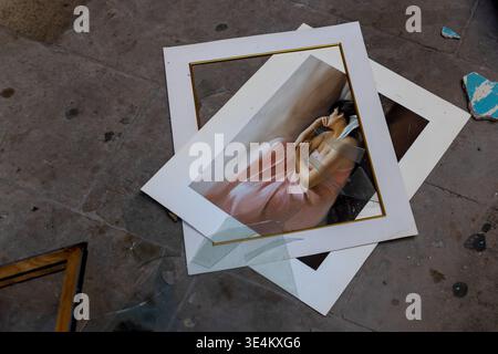 Framed portrait painting lying on a concrete floor with broken glass and scattered frame parts in an abandoned interior. Stock Photo