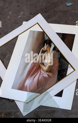 Portrait painting in a white frame lying on a concrete floor with broken glass pieces and stacked backing boards. Stock Photo