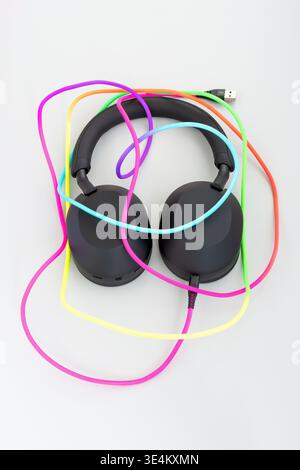 Top view of black over ear headphones with bright colorful braided cables loosely draped around them on a light gray background. Stock Photo