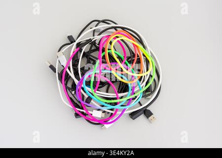 Top view of a tangled assortment of black, white, and brightly colored cables with various connectors on a light gray background. Stock Photo