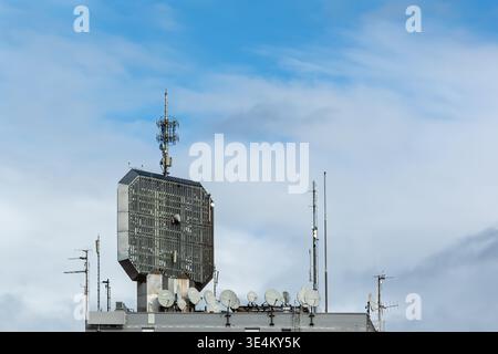 Telecommunications antennas and satellite dishes are installed on a rooftop structure beneath a blue sky with light clouds. Stock Photo