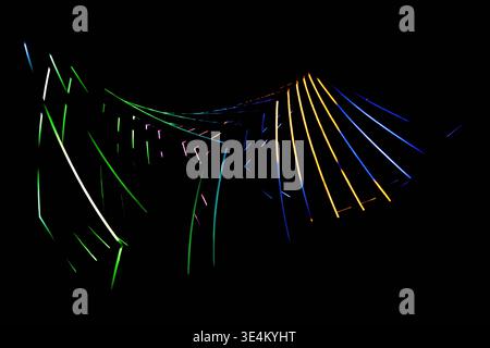 Wide abstract view of curved glowing lines in green, orange, blue and pink on a black background. Stock Photo
