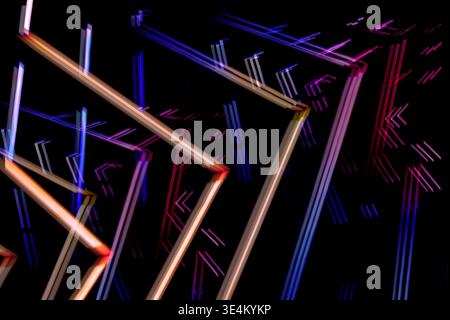 Long exposure abstract image with pink, blue, and orange neon light trails forming zigzag lines on a black background. Stock Photo