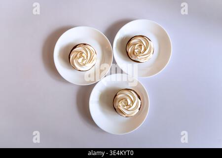 Top view of three small tartlets with toasted meringue served on white plates over a clean white background. Stock Photo